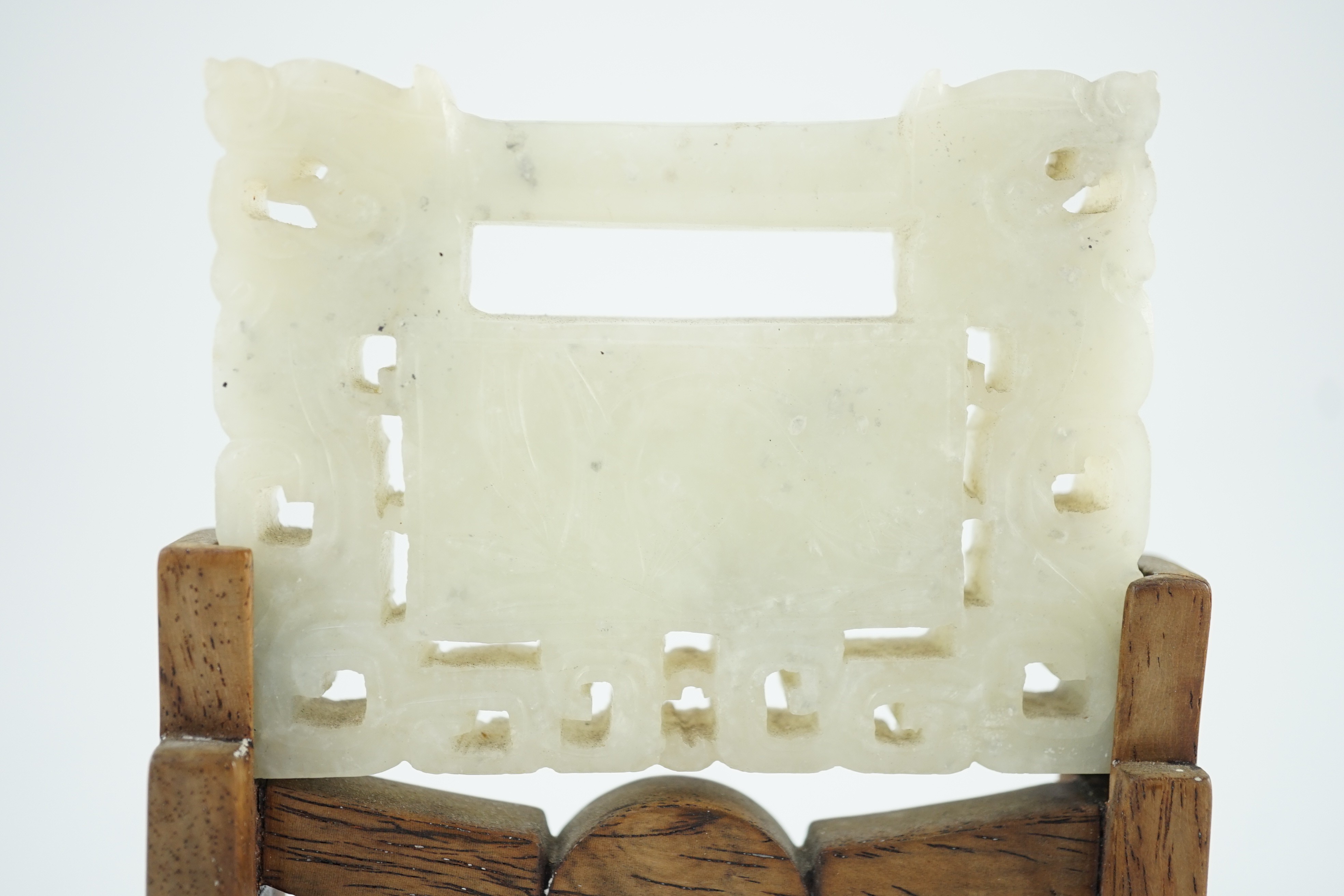 A Chinese speckled white jade ‘lock’ pendant plaque, 19th/20th century, 7.6cm x 5.8cm, wood stand